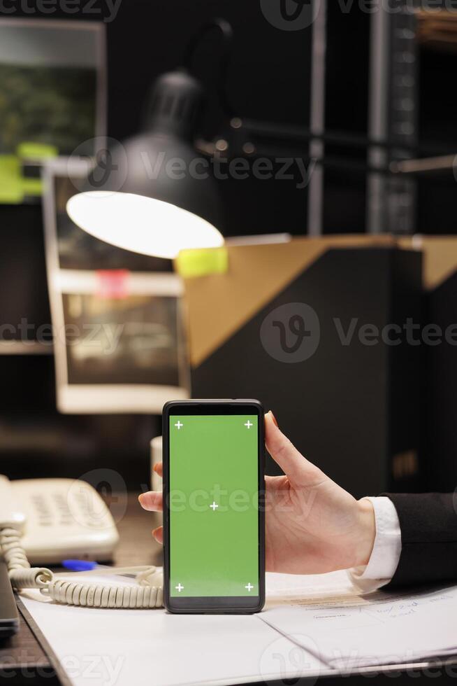 Private detectives showing mobile phone with green screen mock up chroma key isolated display. Criminology employees working late at night at confidential criminal case in evidence room. photo