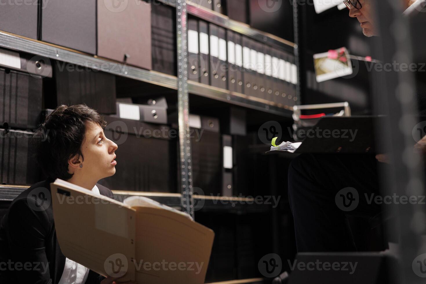 Overworked police officers analyzing confidential files in evidence room, working late at night at criminal investigations. Tired private detectives checking missing person case report photo