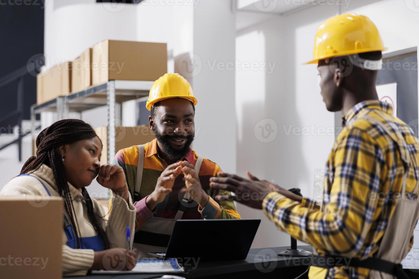 African american postal warehouse coworkers chatting at reception desk. Storehouse package handlers wearing helmets working and managing documentation with manager at counter table photo