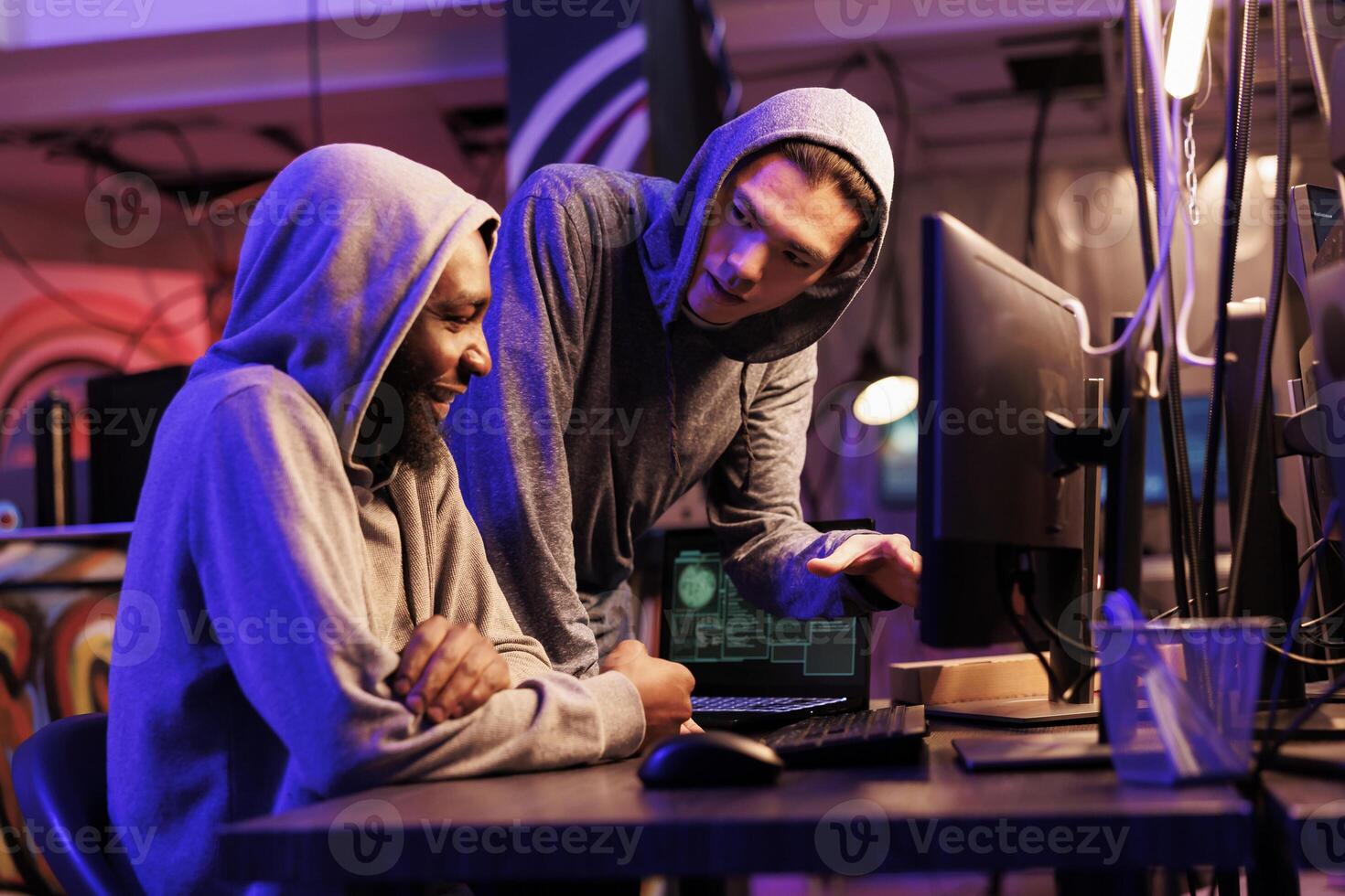 Hackers smiling while cracking encrypted information successfully on computer and working together in hideout place. Two criminals coding illegal malicious software for server hacking photo