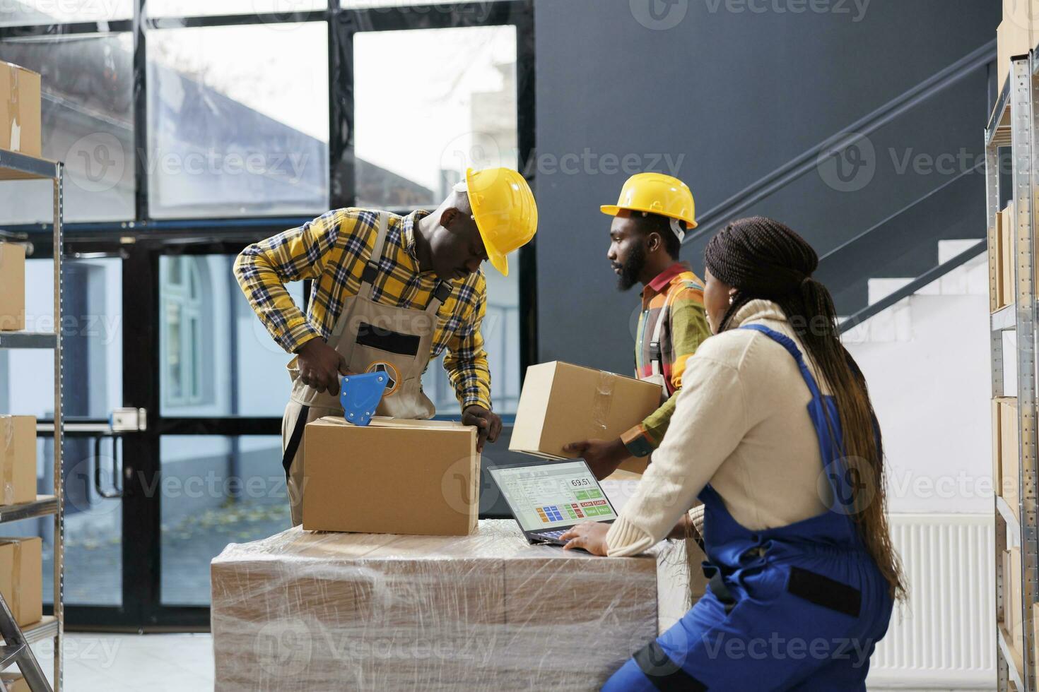 African american warehouse managers team preparing customer order for delivery. All black storehouse employees packing cardboard box with sticky tape and checking goods list on laptop photo