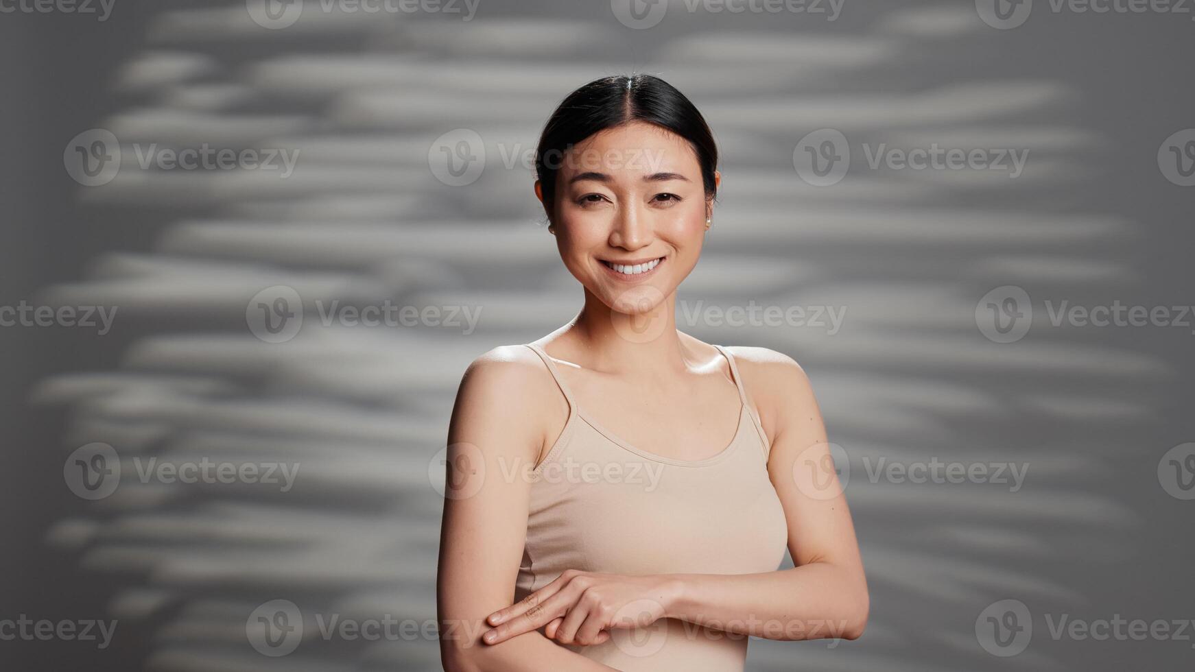 Sensual radiant adult applying body cream on camera, advertising self love and body positivity. Asian woman with bare luminous skin using moisturizer and serum for skincare routine ad. photo