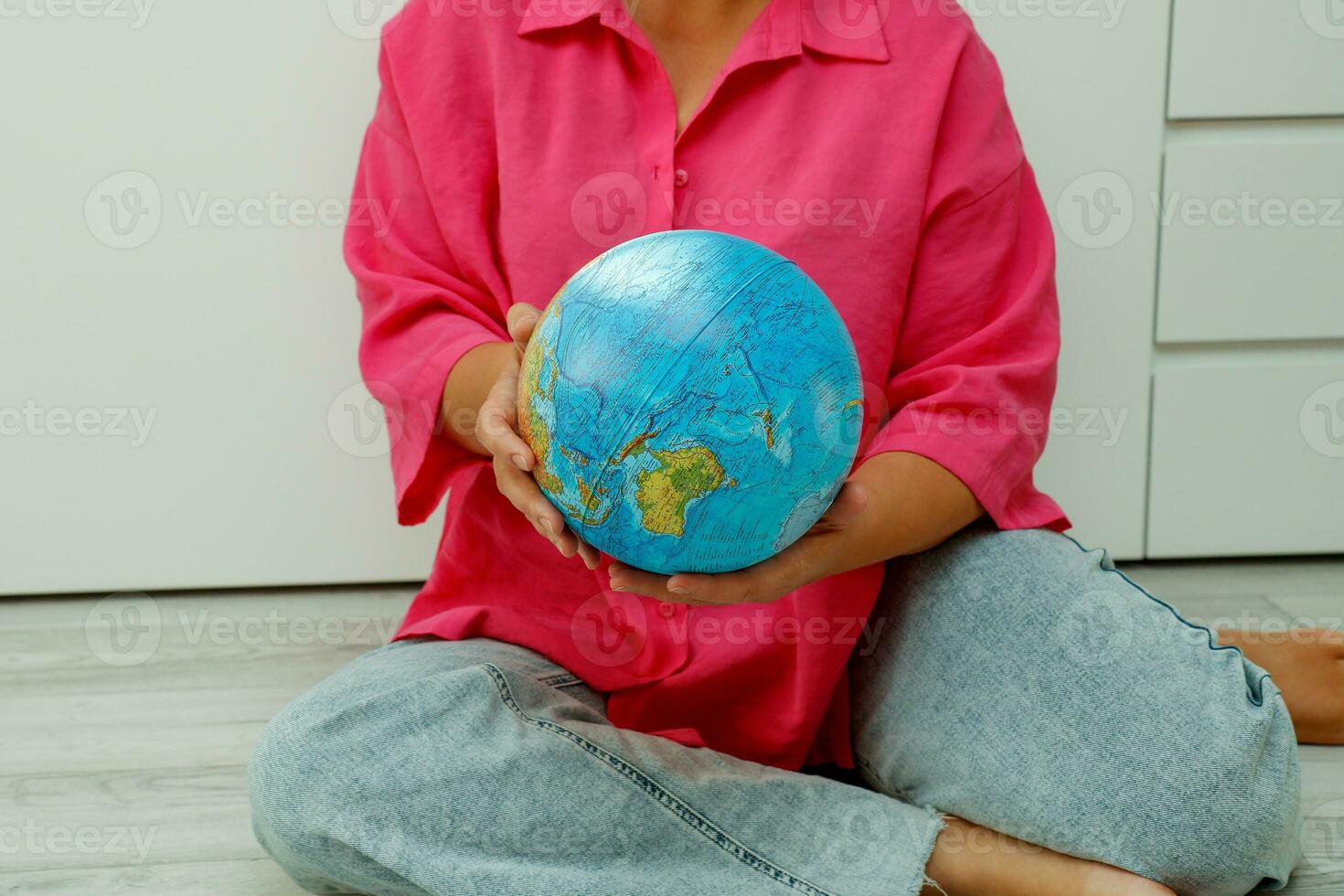a girl in a crimson shirt and jeans sitting on the floor holds a globe in her hands photo