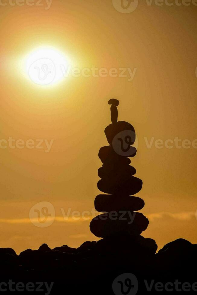 a stack of rocks is silhouetted against the sun photo