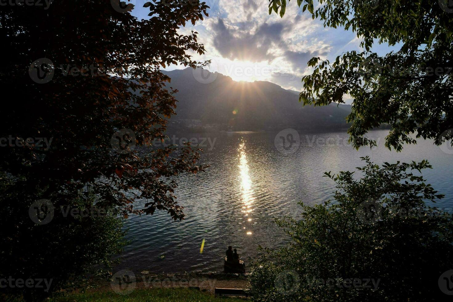 the sun is setting over a lake with trees photo