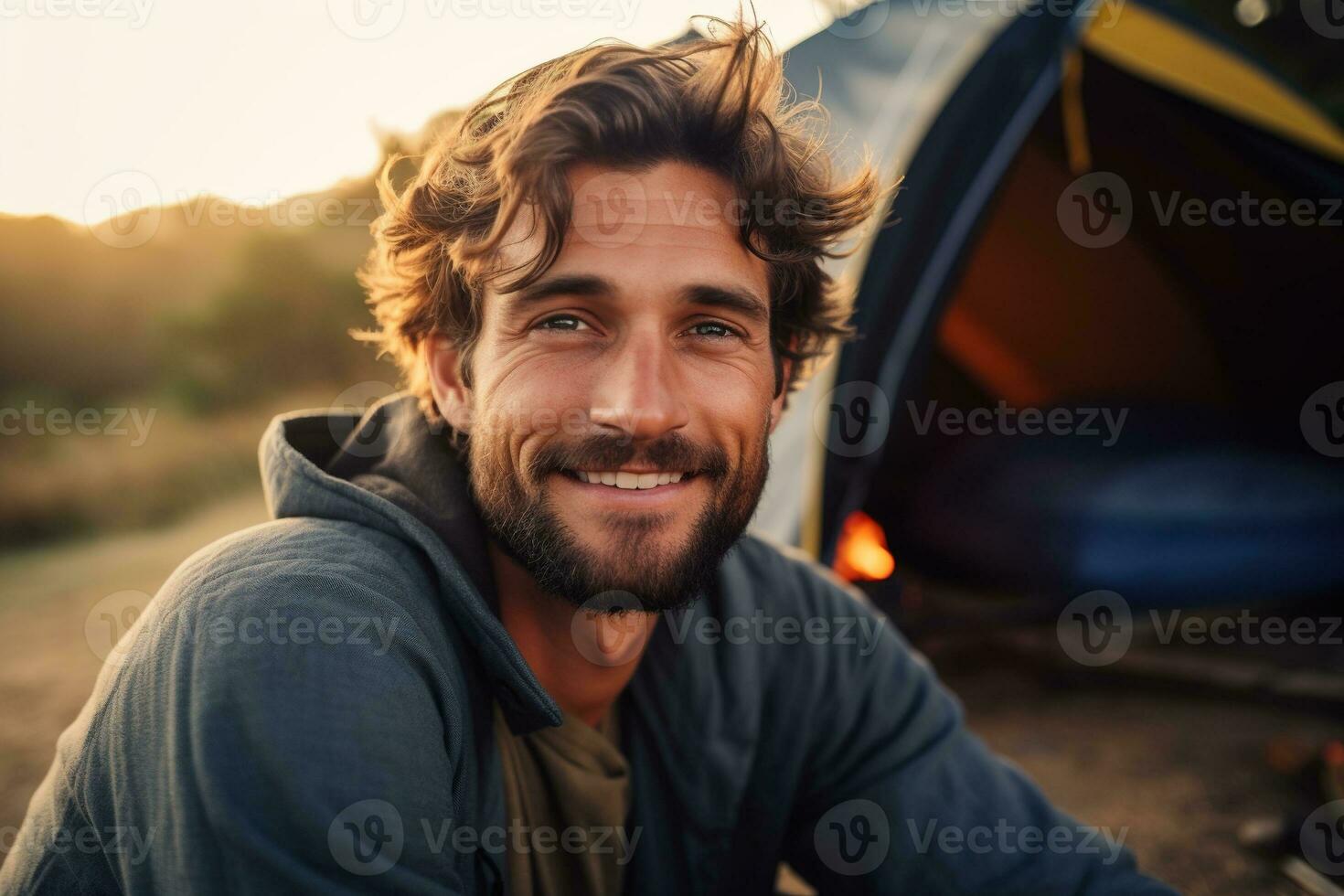 Portrait of man looking at camera while near camping tent at sunset AI generated photo