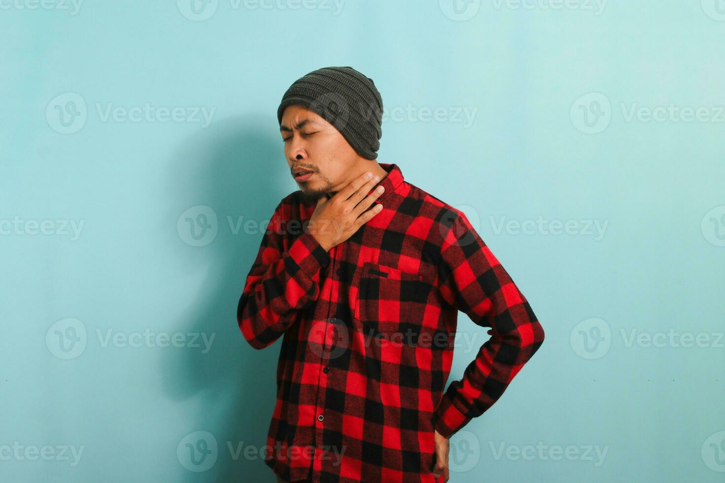 indispuesto joven asiático hombre participación su cuello, sufrimiento desde un dolorido garganta, aislado en azul antecedentes foto