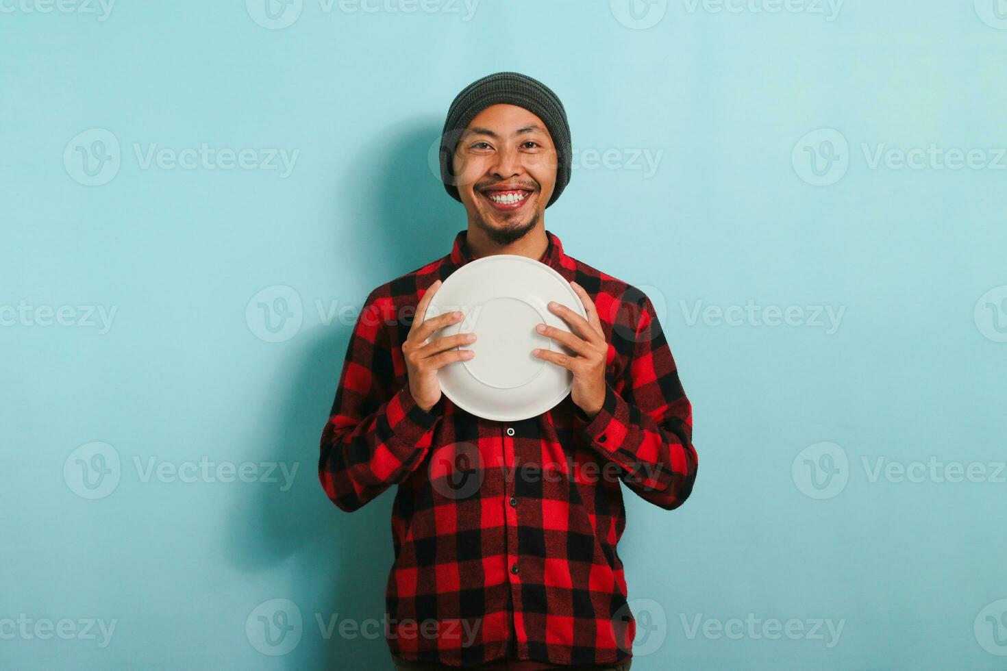contento joven asiático hombre es sonriente mientras participación un vacío blanco lámina, aislado en un azul antecedentes foto