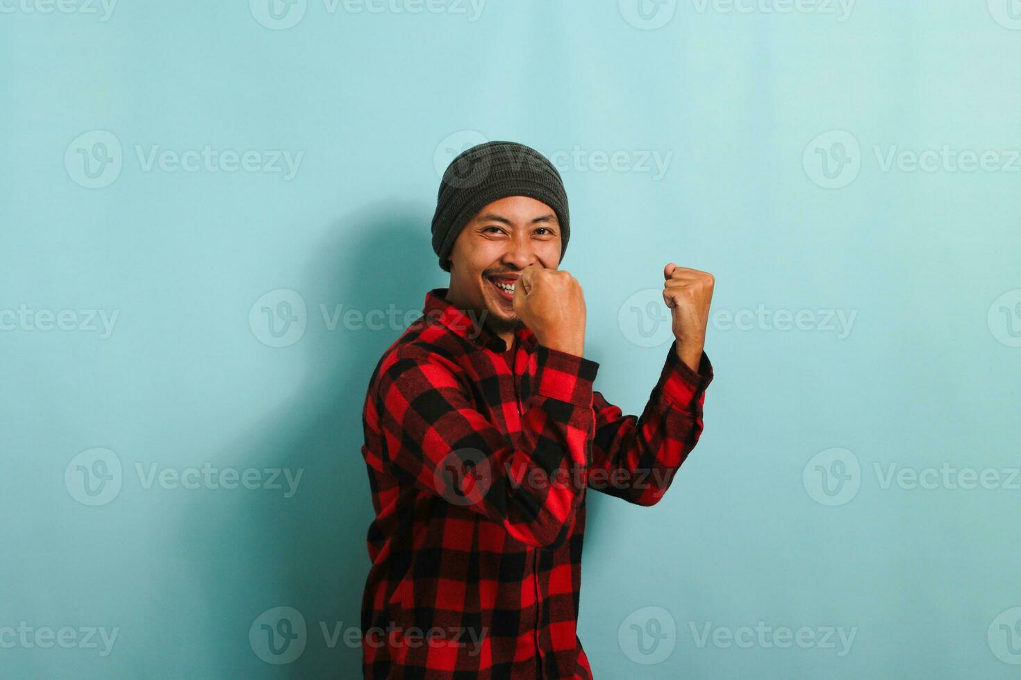 Excited young Asian man rejoicing, saying YES with fist pump gesture, isolated on blue background photo