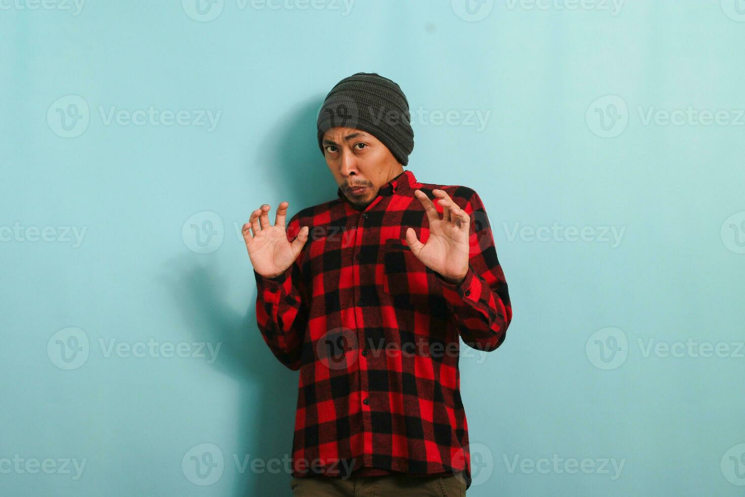 Ew, It's so gross. An annoyed young Asian man with a beanie hat and a red plaid flannel shirt is repulsed by something, displaying a disgusted expression while standing against a blue background photo