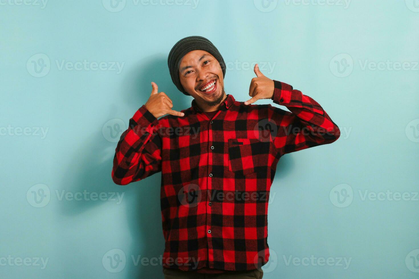 An excited young Asian man makes a CALL ME gesture with his hand, isolated on a blue background photo