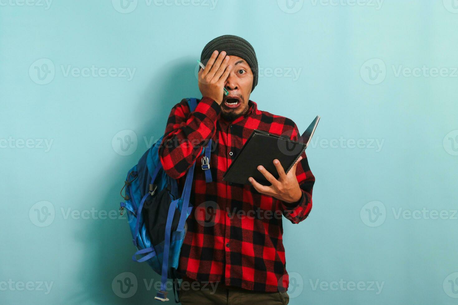Young Asian student looks shocked after realizing he forgot to study before the exam blue background photo