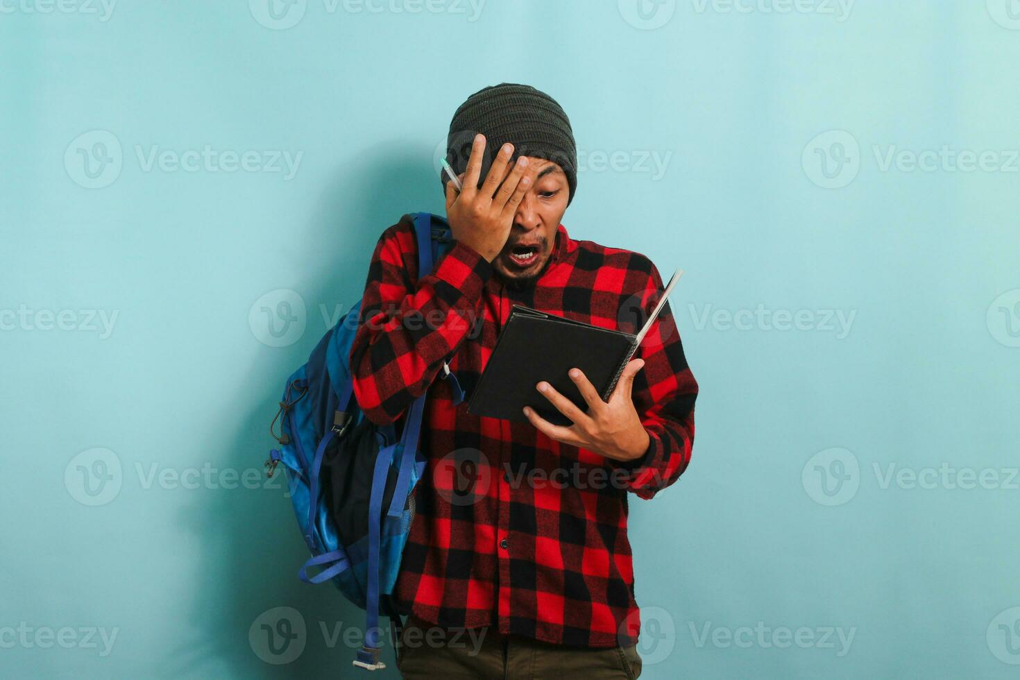 Young Asian student looks shocked after realizing he forgot to study before the exam blue background photo