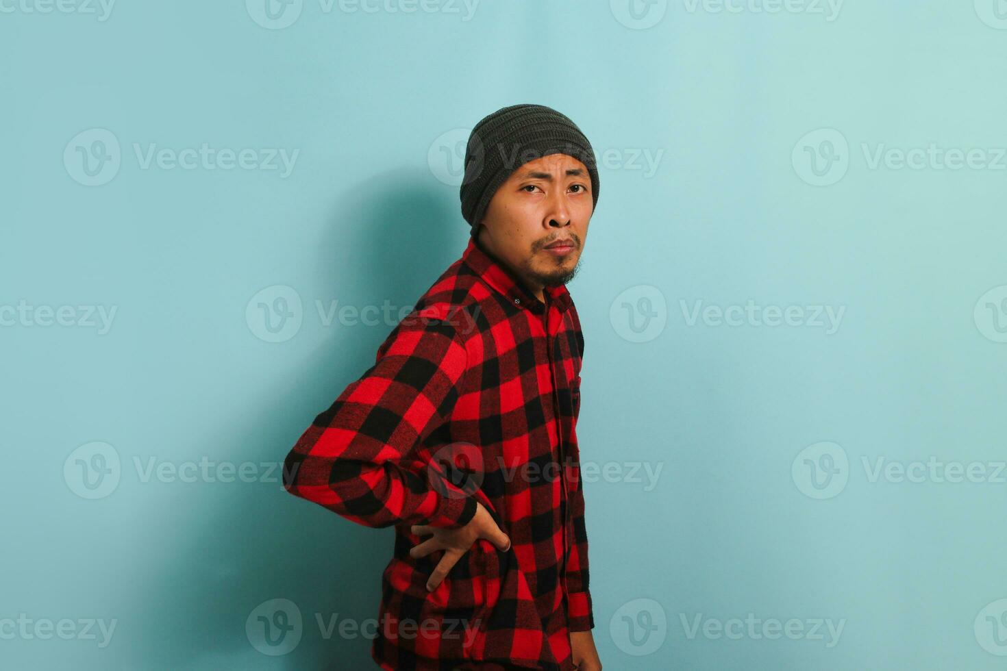 joven asiático hombre es sufrimiento desde un dolor de espalda, experimentando espalda dolor, aislado en un azul antecedentes foto