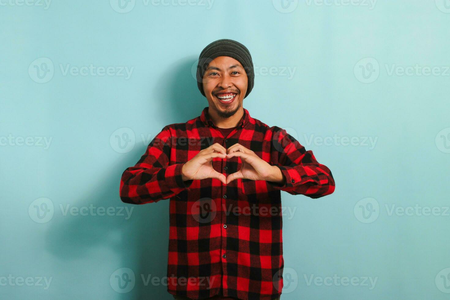 Smiling young Asian man shows a love gesture with his hand while standing against a blue background photo