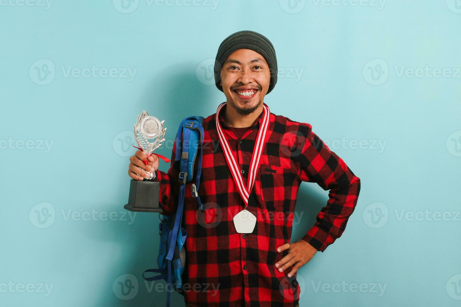 Happy young Asian man student showing a medal and trophy, isolated on a blue background photo