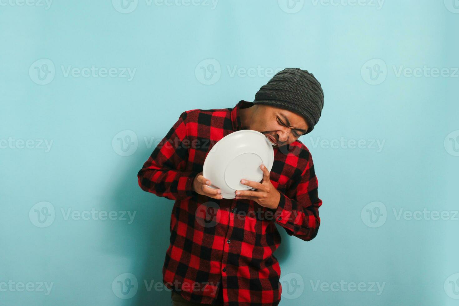hambriento joven asiático hombre picaduras un vacío blanco lámina, aislado en un azul antecedentes foto