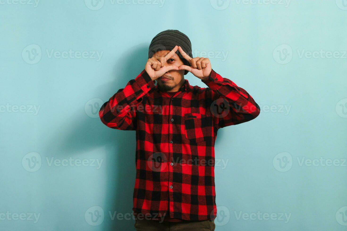 Young Asian man with beanie hat and red plaid flannel shirt making a triangle gesture with palms, symbolizing the environment protection, recycling, and reusing concept, isolated on a blue background photo