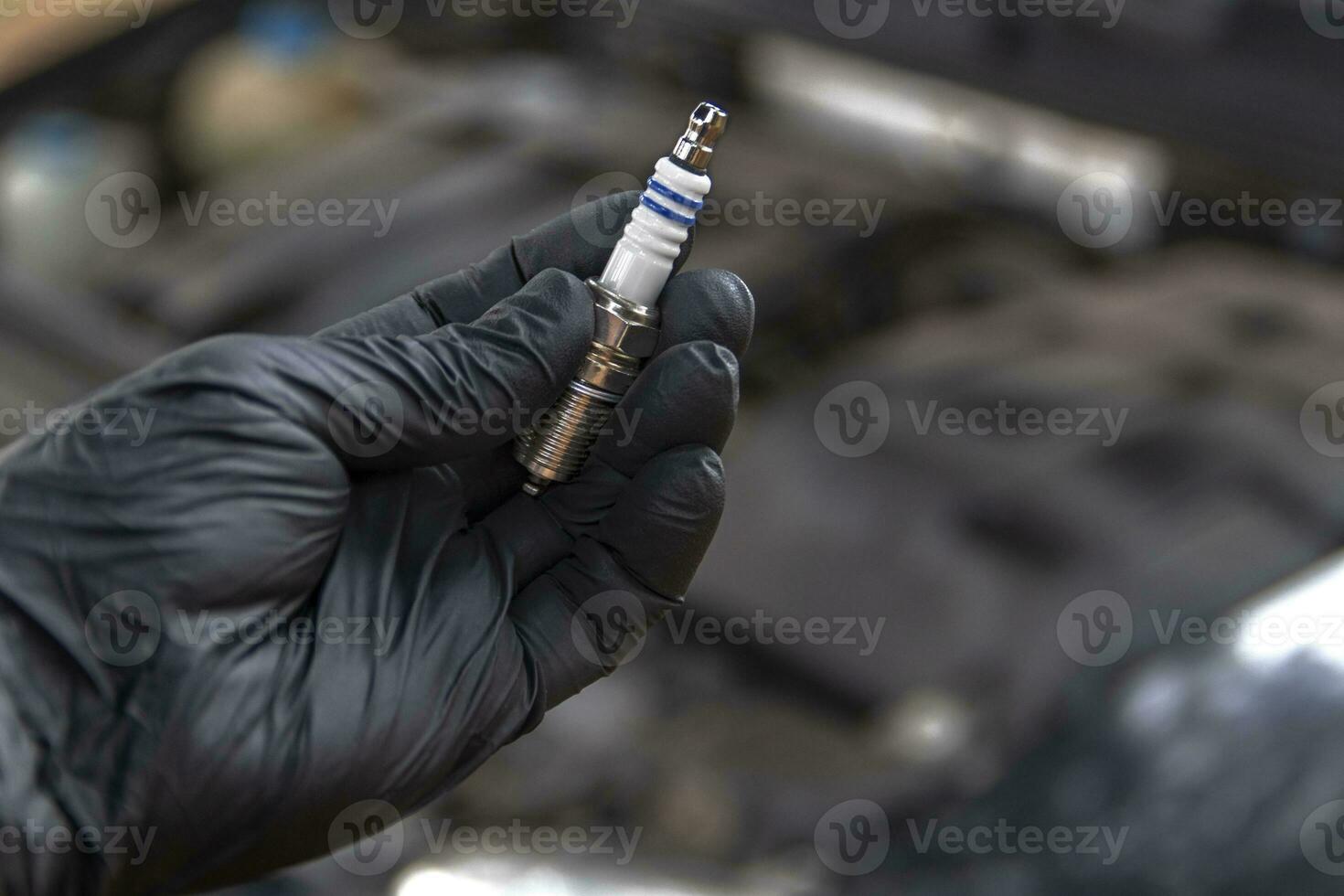 A black gloved hand holding a car spark plug. Vehicle maintenance concept. photo