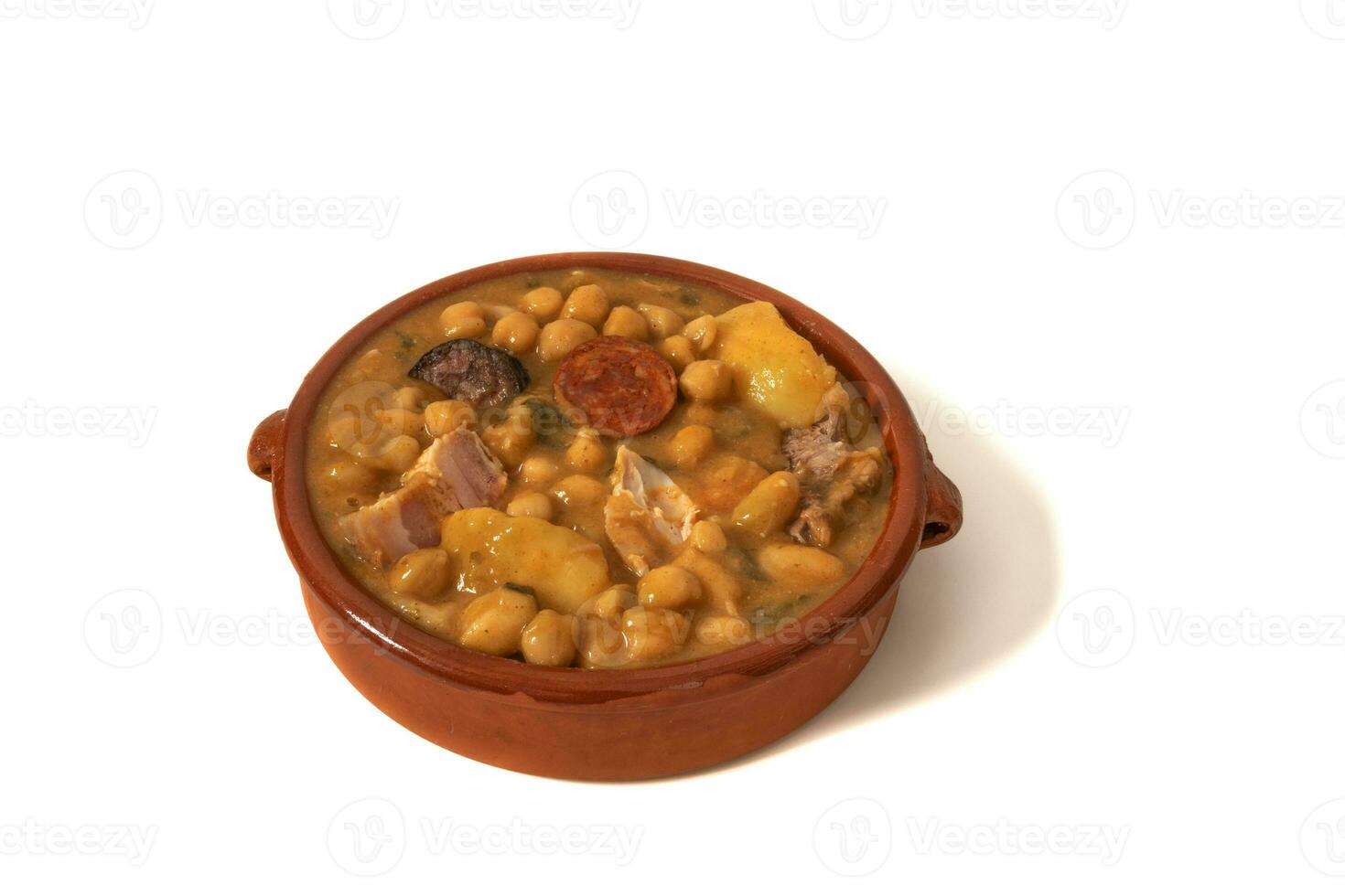 A chickpea soup in a clay bowl, isolated on a white background. This comforting chickpea stew combines traditional flavors such as chorizo, black pudding and vegetables, creating a aromatic dish. photo