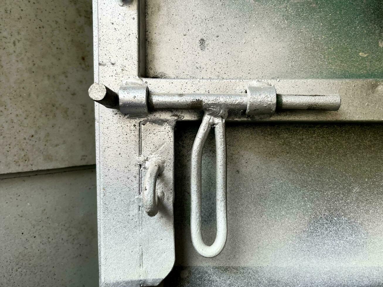 Metal iron sliding lock with long handle for locking gate door. Industrial door interior close up object isolated on grungy and textured spray painted metal door. photo