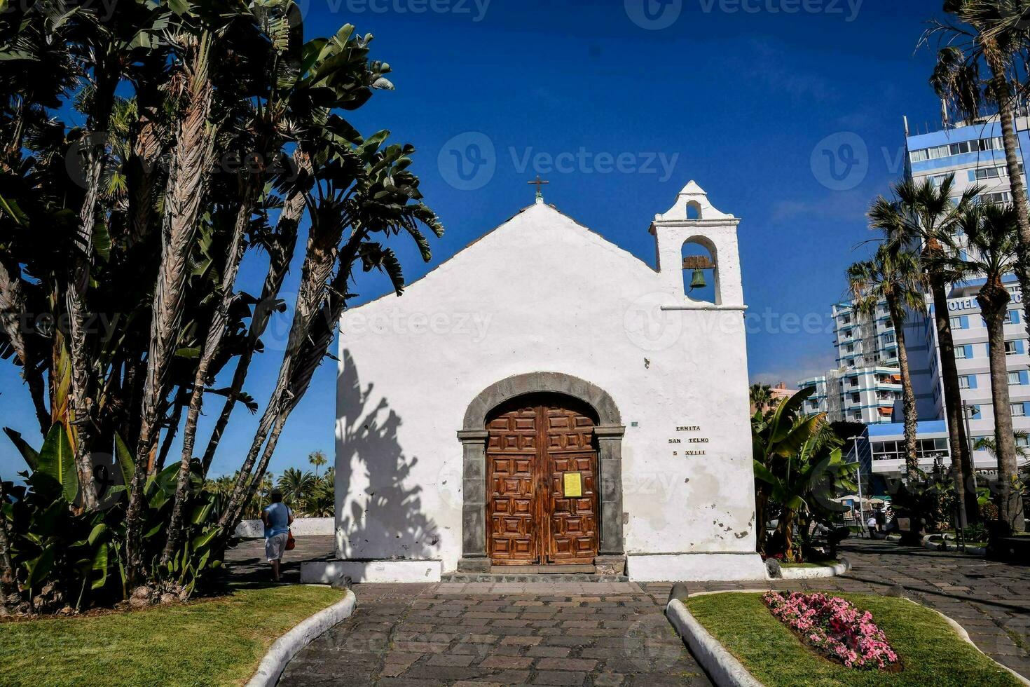 un pequeño blanco Iglesia con palma arboles y flores foto