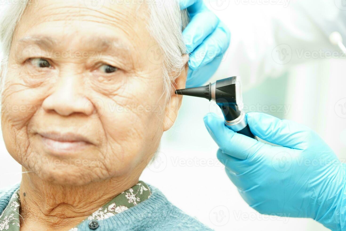 Otolaryngologist or ENT physician doctor examining senior patient ear with otoscope, hearing loss problem. photo