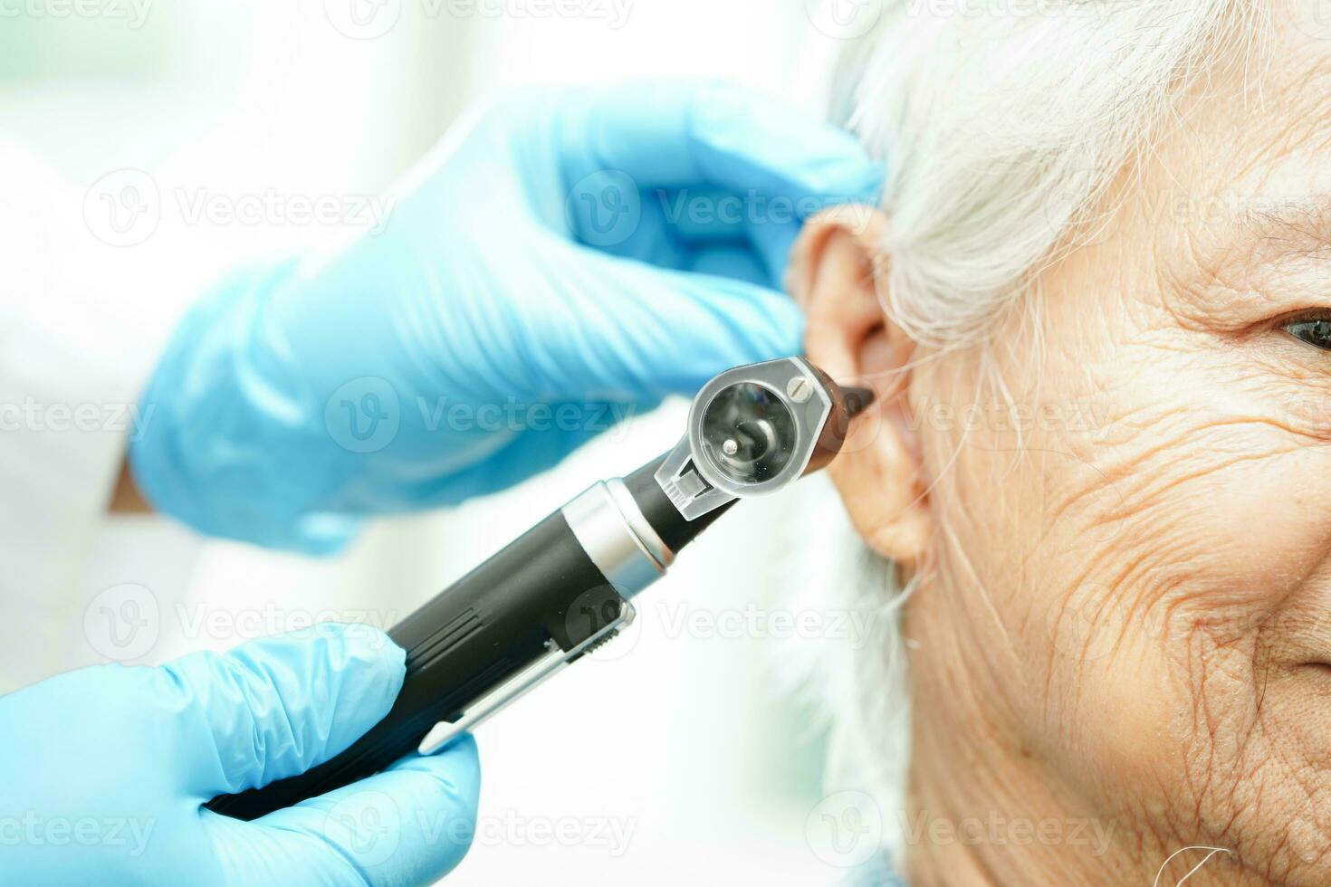 Otolaryngologist or ENT physician doctor examining senior patient ear with otoscope, hearing loss problem. photo