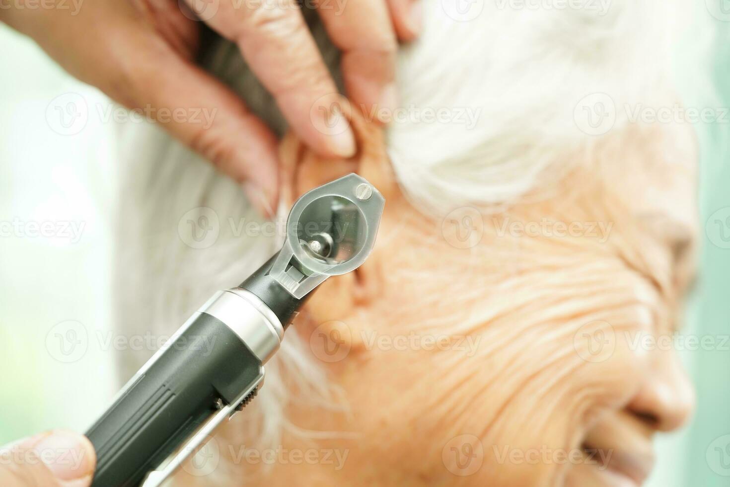 Otolaryngologist or ENT physician doctor examining senior patient ear with otoscope, hearing loss problem. photo