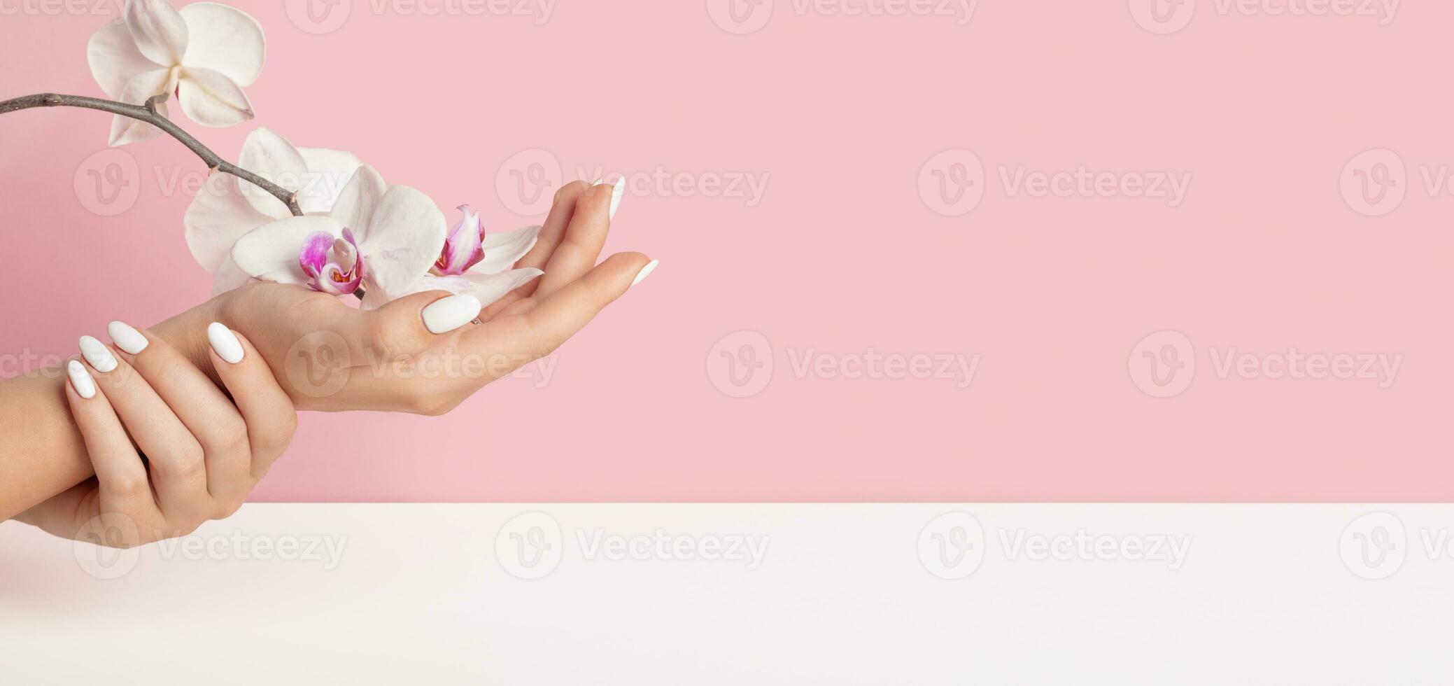 sutil dedos hermosa joven mujer manos con blanco uñas en un rosado antecedentes orquídea flores foto