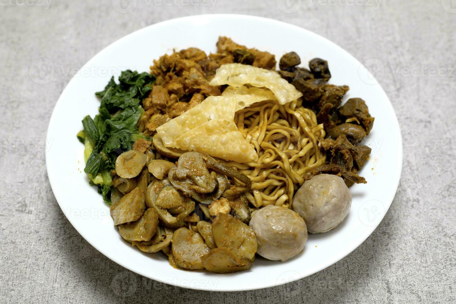 Delicious and Tasty Mie ayam or Mie Yamin or Yamin Noodle with chicken meat, vegetable, Pangsit Goreng, Pangsit rebus and meatballs on white plate photo