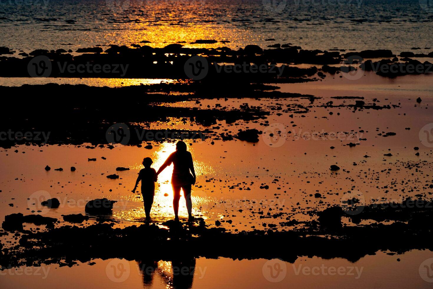 Mother and son walking hand in hand by the sea as the sun sets. photo