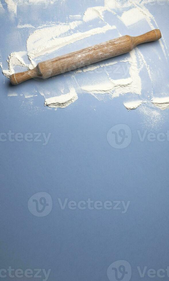 Sprinkled wheat flour and wooden rolling pin on blue background photo