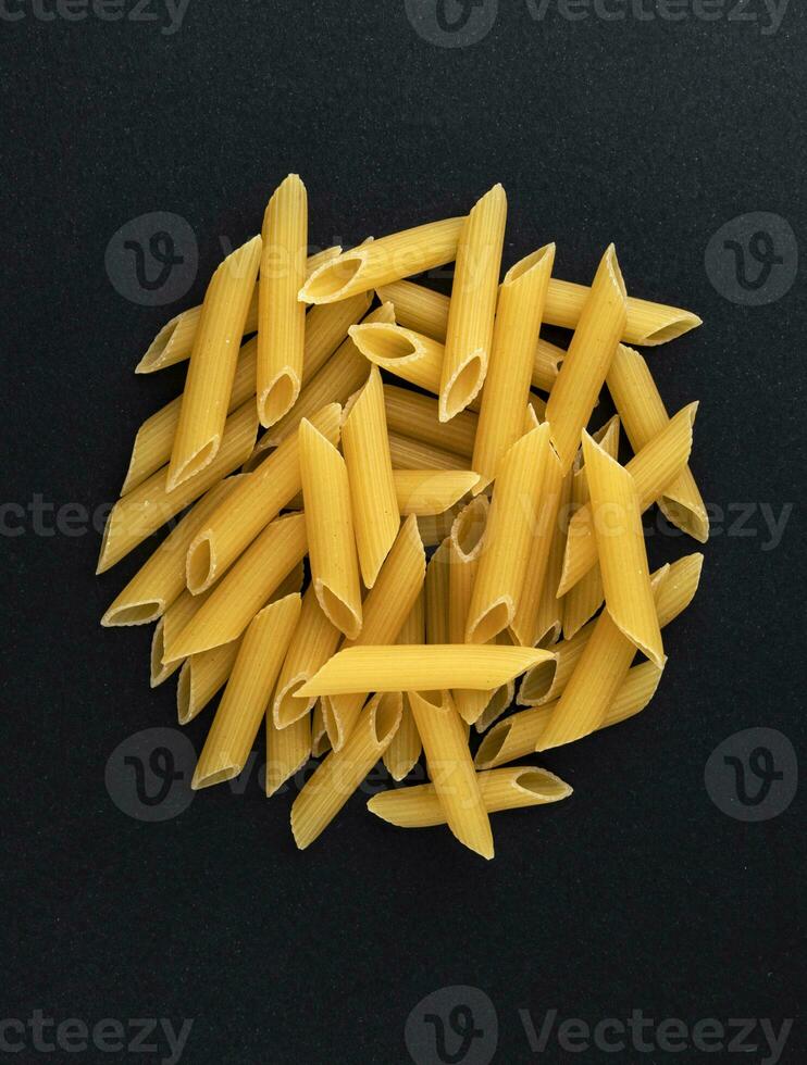 Raw penne rigate pasta isolated on black background, top view photo