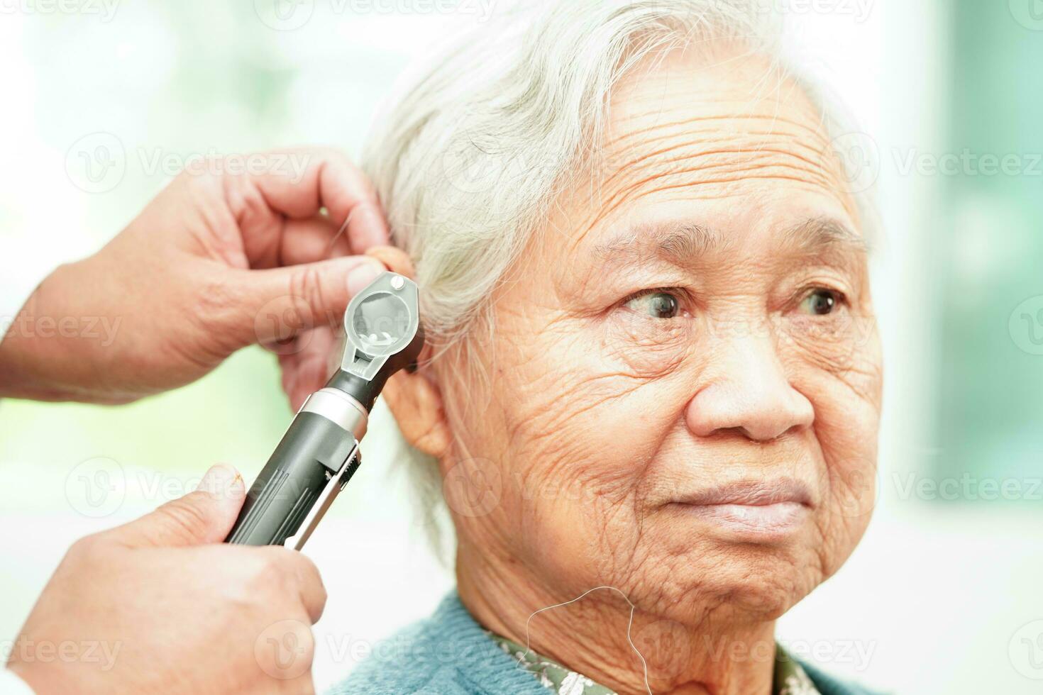 Otolaryngologist or ENT physician doctor examining senior patient ear with otoscope, hearing loss problem. photo