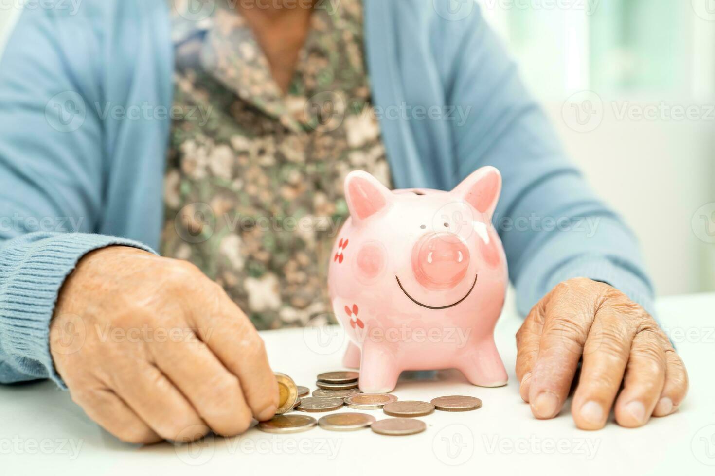 asiático mayor mujer poniendo moneda dentro rosado cerdito banco para ahorro dinero y seguro, pobreza, financiero problema en Jubilación. foto