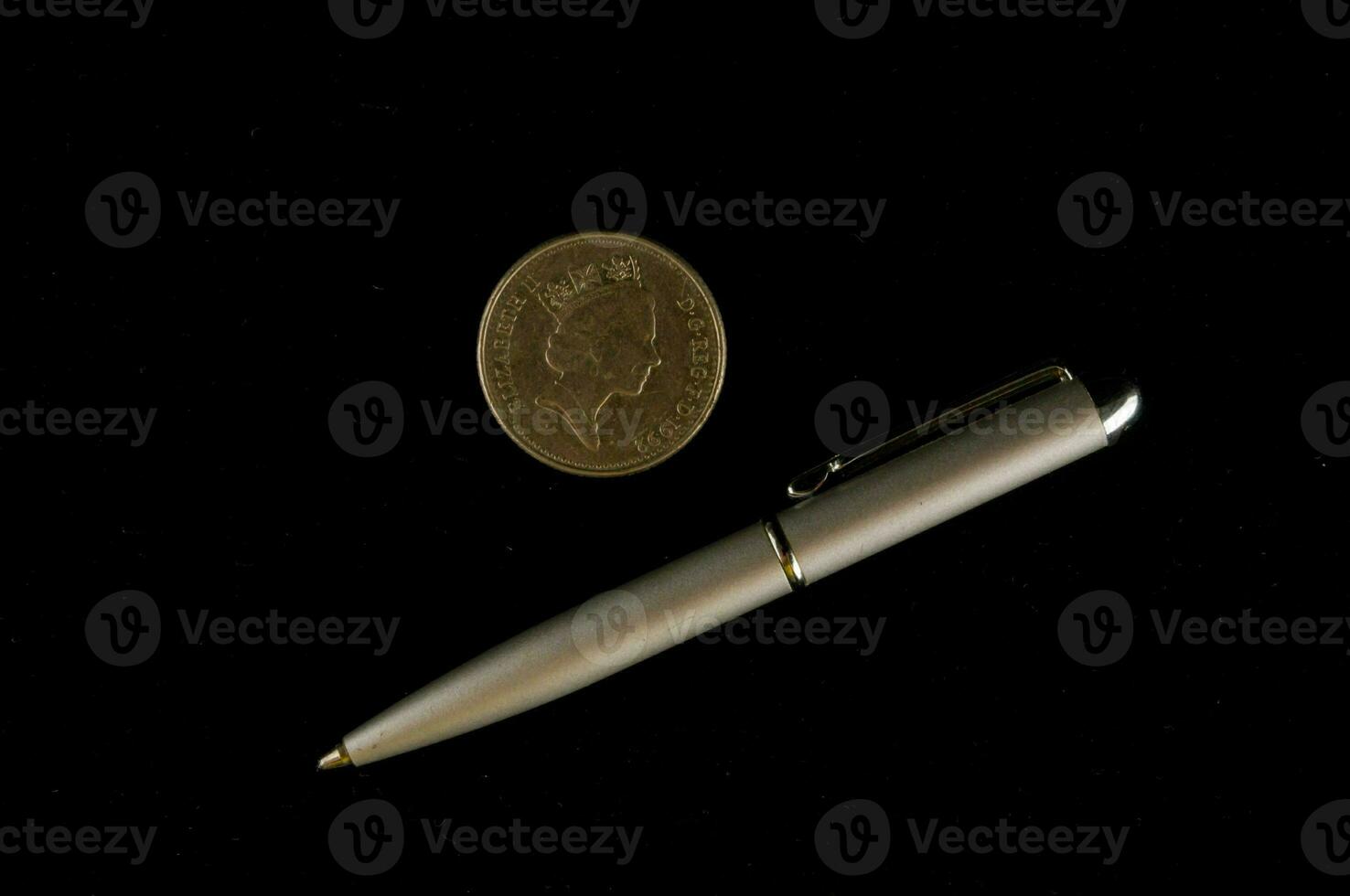 a silver pen and a coin on a black background photo