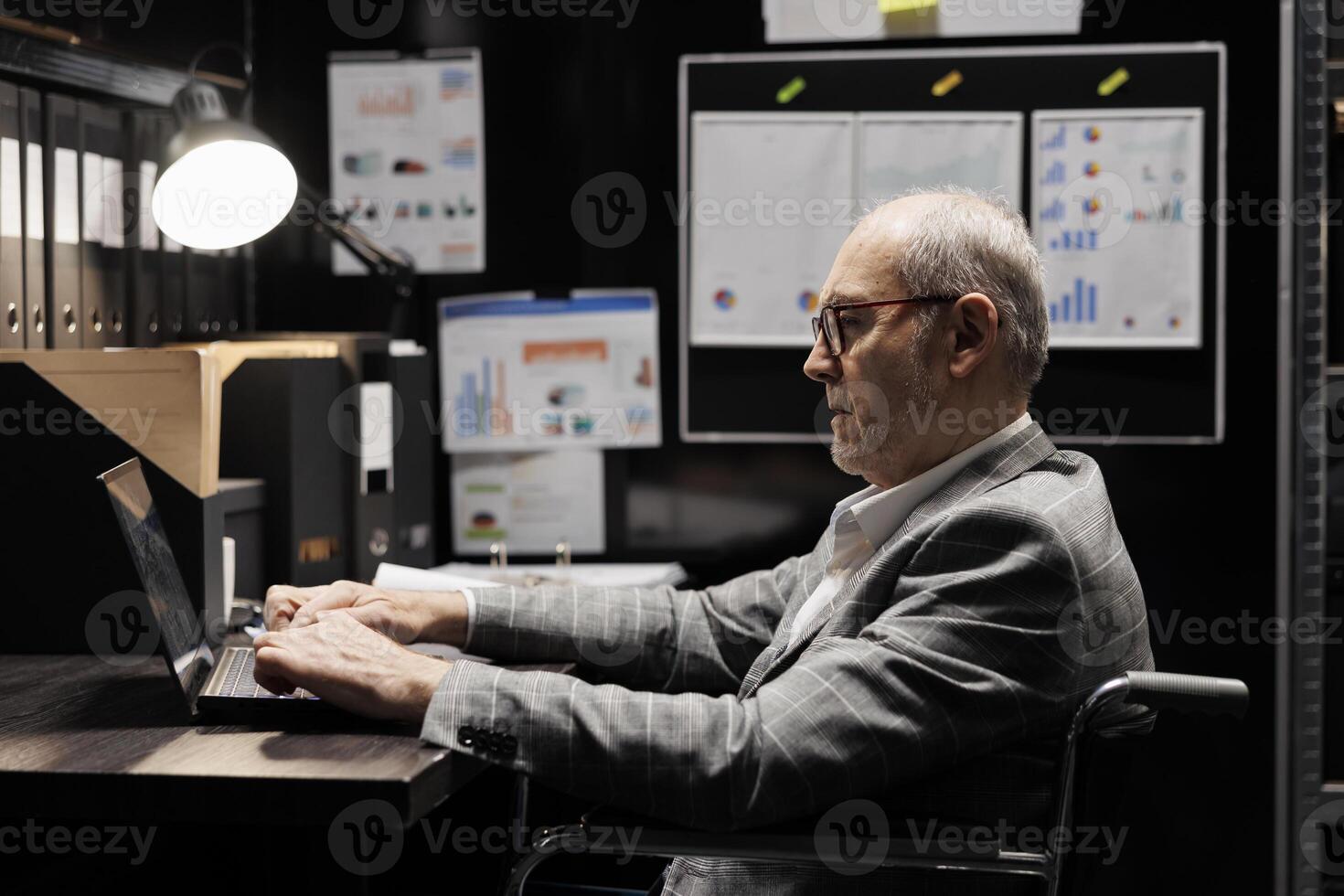Senior manager who is paralyzed in wheelchair checking annual profit revenue, doing objective completion evaluation before business meeting. Elderly executive with paraplegia in bureaucratic workplace photo