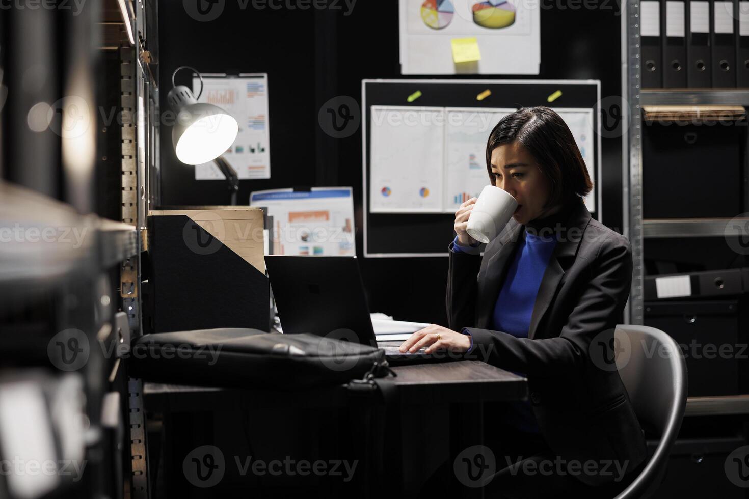 Accountant businesswoman employee enjoying mug of coffee starting her shift in business administration office workplace. Asian executive in archival repository filled with folders and flowcharts photo