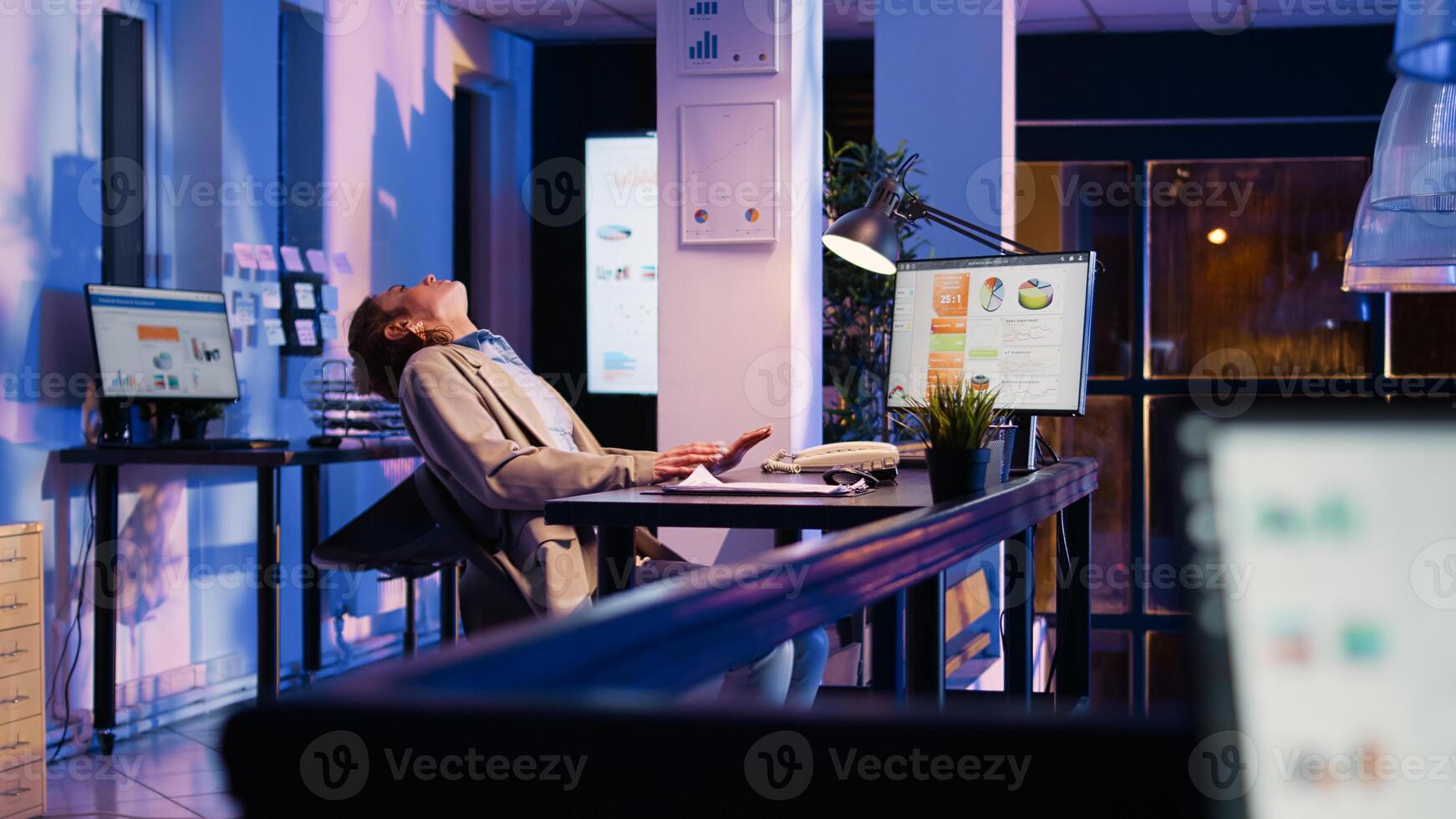 Business woman falling asleep at office desk, working after hours and yawning. Executive assistant feeling exhausted in corporate space, trying to work on financial project report. Handheld shot. photo