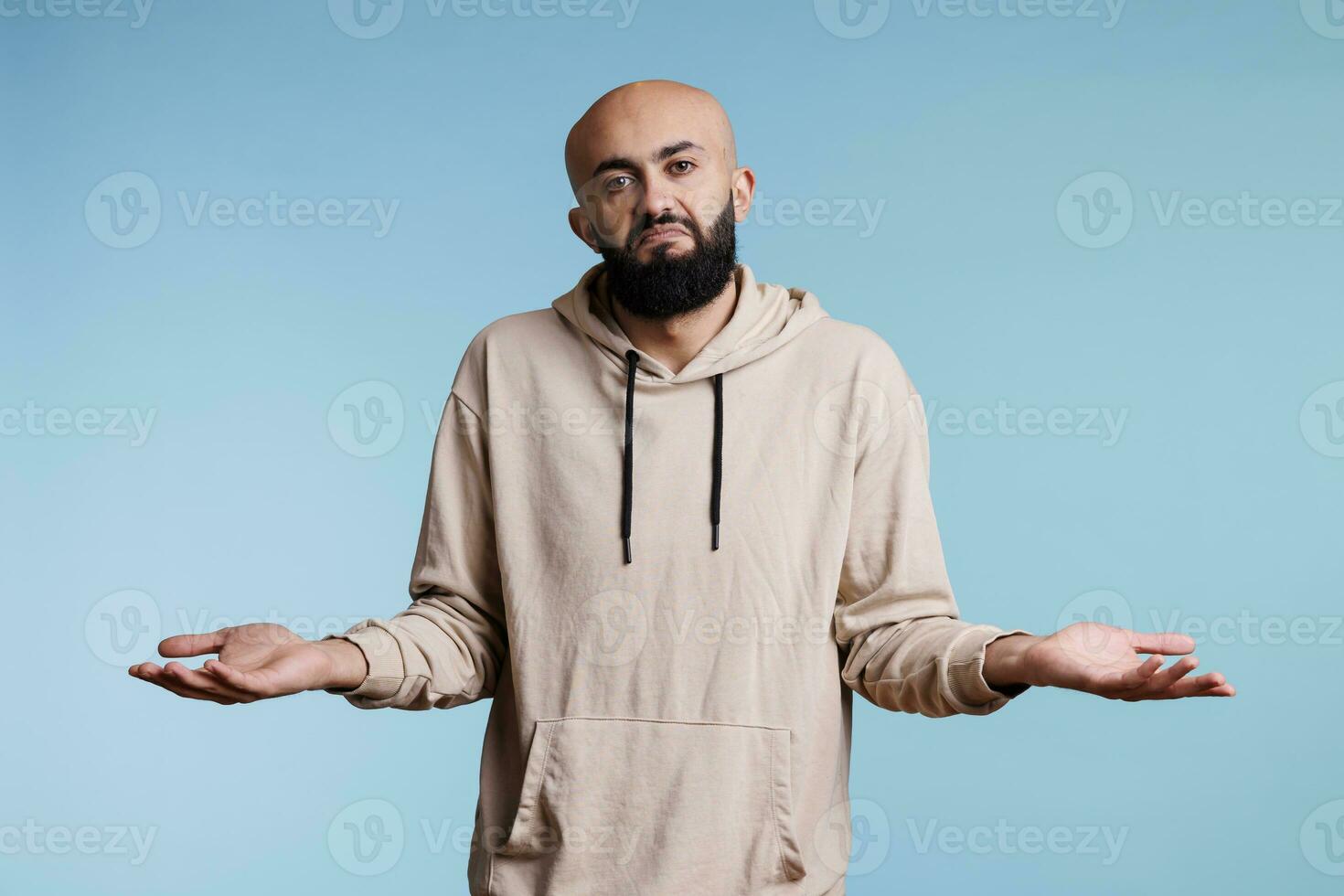 Arab man with spread arms and puzzled expression showing do not know gesture portrait. Young bald beared person looking at camera with confused emotions while shrugging shoulders photo