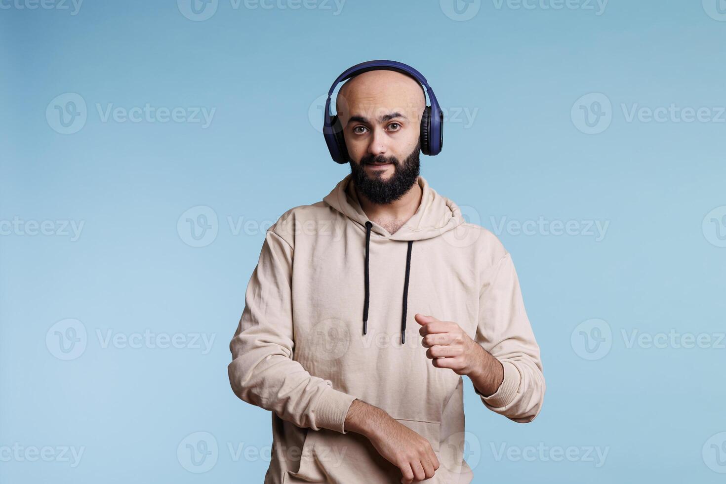 Arab man listening to music in headphones and making moves with hands portrait. Relaxed young person wearing wireless earphones dancing while enjoying song and looking at camera photo