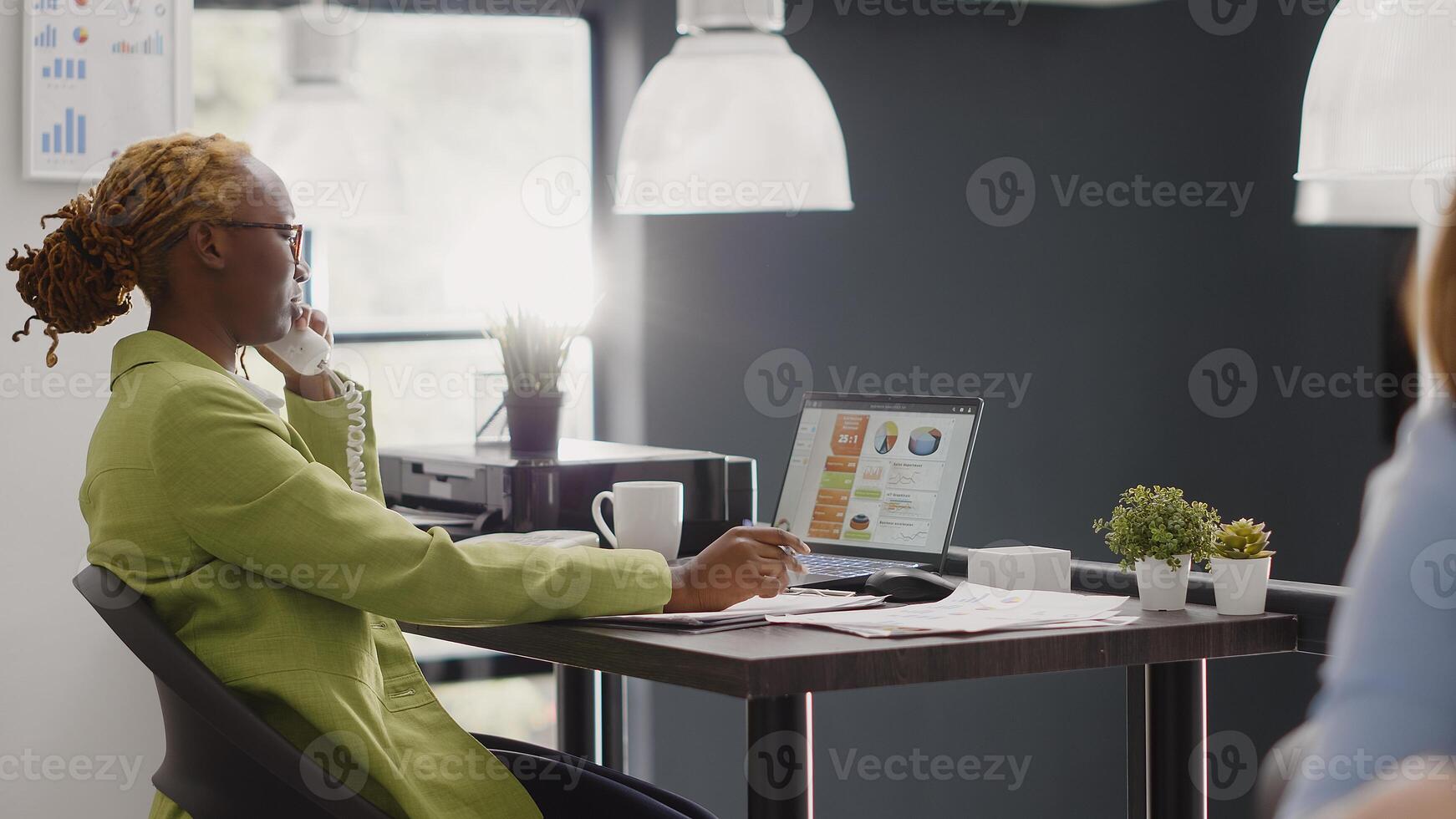 African american manager using landline phone to call people from management department, working on executive report. Young adult using telephone with cord in business office. photo