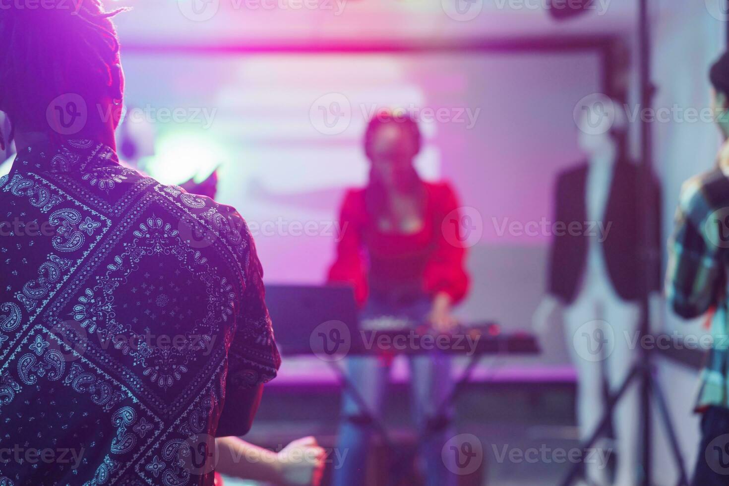 People watching live electronic music concert on stage with spotlights in nightclub. African american musician performing using dj controller in nightclub on blurred background photo