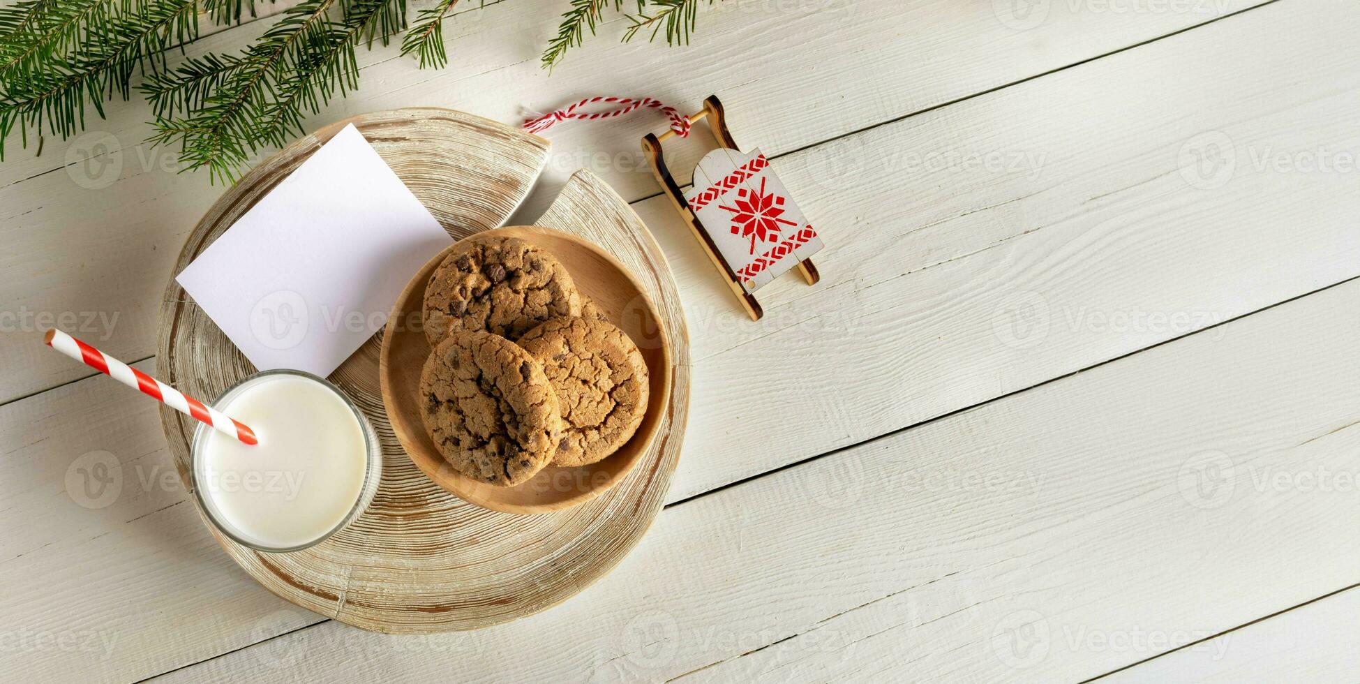 Top view Christmas composition. Glass milk, cookies, Santa's sleigh, empty note, white wooden table. photo