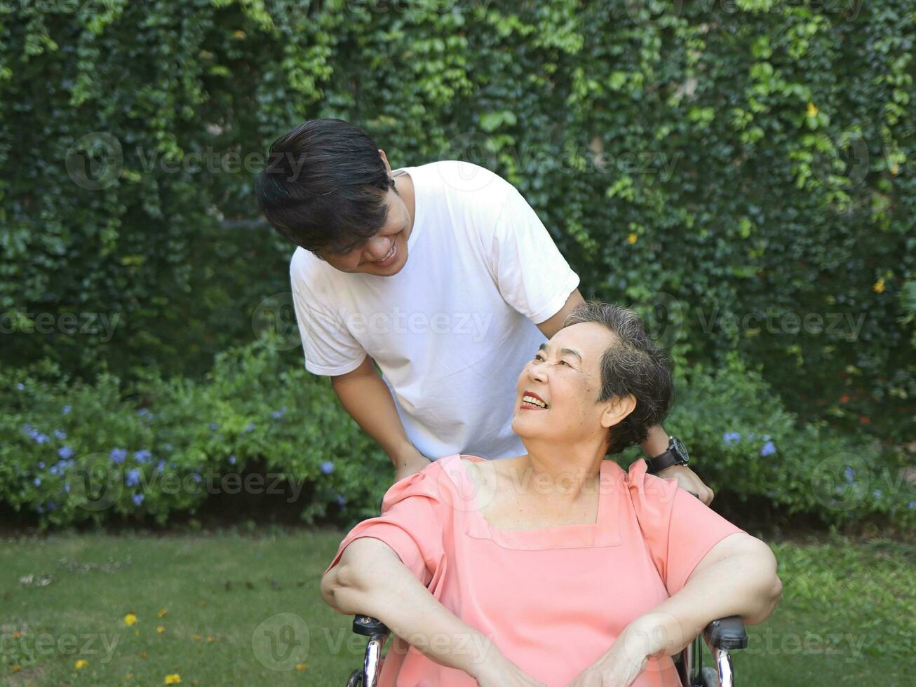 asiático mayor mujer sentado en silla de ruedas con su hijo en el jardín. foto