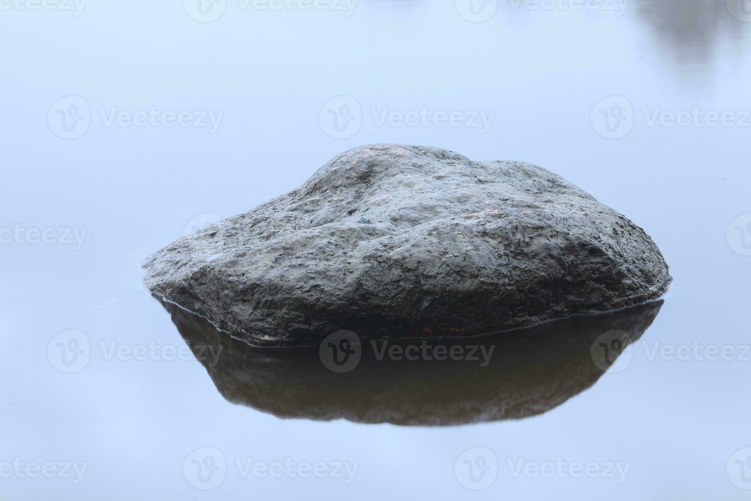 large smooth boulder rises above the surface of the river and is reflected in the mirror water photo