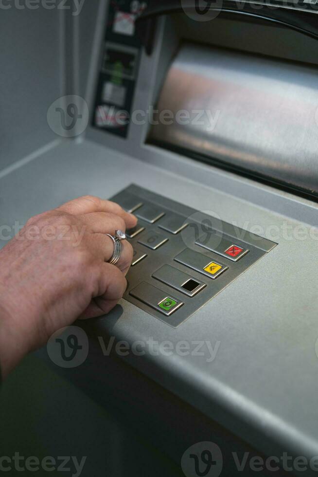Middle aged woman using ATM pressing the PIN security on the number pad. photo