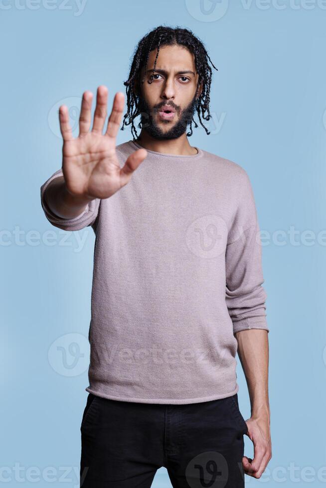 Arab man showing no gesture with hand and telling to stop while looking at camera. Person making prohibition sign with arm and standing in confident pose with serious face expression photo