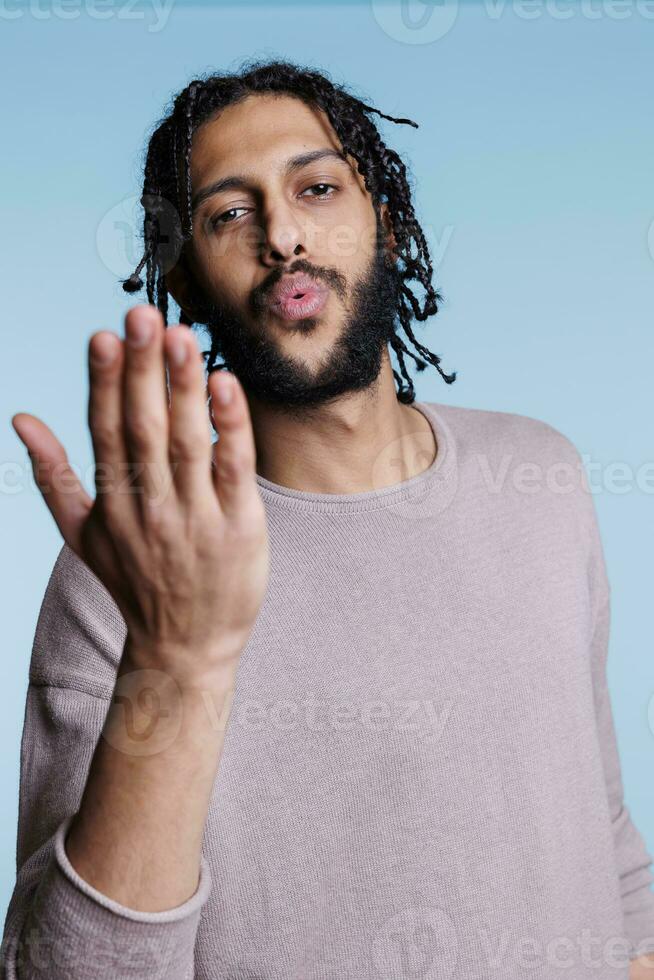 Attractive arab man blowing flirty air kiss and looking at camera with charming facial expression. Handsome young model sending love and affection while flirting portrait photo